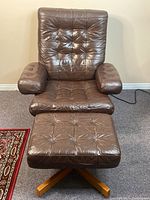 Front view of chair and ottoman showing tufted leather upholstery, padded armrests and wood base