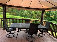 Overall view of metal patio table and four swivel chairs under canopy