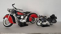 Both motorcycle models displayed side by side on a white surface. The larger red and black Indian Chief is positioned at front left, the gray Honda Goldwing GL 1800 is behind it to the right.