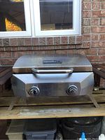 Front and top views of the NextGrill portable propane barbecue showing stainless steel body with two control knobs and attached propane tank.