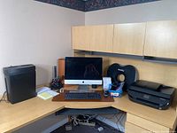 Corner desk setup showing Apple iMac on integrated stand with keyboard and mouse, HP OfficeJet 4650 printer, Fellowes shredder and assorted office supplies