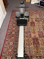 Full view of the rowing machine on a carpet showing frame, foot pedals, and seat