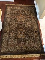 Full view of rectangular area rug with floral/botanical intricate pattern in earth tones, visible wear spots.