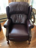 Front view of burgundy leather wing back recliner with visible carved claw feet and nailhead trim