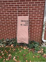 Full view of metal blanket ladder with hanging beige blanket outdoors against a brick wall.