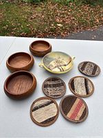 Photo showing three wooden bowls, one ceramic bowl with painted scene, and six Turkish rug coasters on white table.