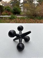 Photo showing front side of black cast iron jacks shaped paper weight with four spherical ends and a central prong.