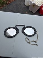 Full view of the vintage cast iron spectacle mirror with chain placed on a white table outdoors.