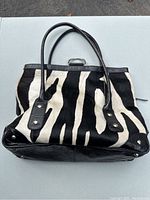 Front and top side view of zebra print leather purse with black leather straps and silver hardware on black leather trim corners.