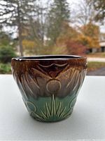 Front view of small McCoy ceramic planter with brown and green glaze and embossed botanical design.