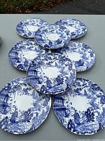 Eight blue and white china plates arranged on a table, showing the Mikado pattern by Royal Crown Derby with Asian figures, pagodas, and garden scenery.