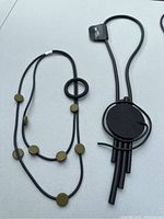 Two abstract foam necklaces on a white surface, one with green wood-like dots, the other with a large circular black pendant and tubular elements