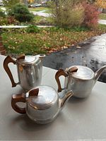 Image showing three Piquot Ware aluminum alloy teapots with wood handles grouped together on a flat surface with outdoor background