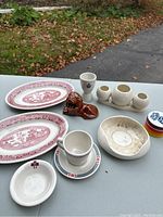Photo showing all ceramic items on table outdoors with autumn leaves background, including dishes, vase, egg holder, and figurine