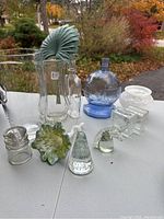 Various clear and colored glass items displayed on a table outdoors with autumn foliage in the background.
