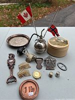 Photo showing the assortment of metal items including music boxes, flags, bottle openers, weight, and decorative pieces on a table outdoors