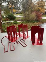 Two sets of red metal bookends displayed on a table outdoors with a fall background.