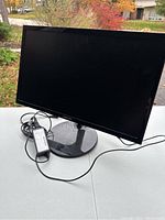Front view of Samsung monitor displaying the screen with its stand and power adapter connected, placed on a table outside.