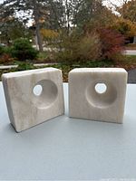 Two square stone book ends positioned to show front with circular hole in center.