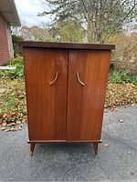 Front view of closed vintage mini wood bar cabinet showing two doors with curved handles and tapered legs.