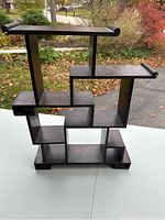 Front view of brown wood decorative stand with multiple compartments and shelves, showing geometric design and staggered shelves