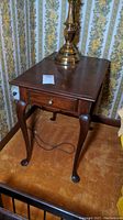 Wooden end table with drawer and curved legs, lamp on top, showing style and construction.