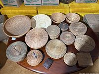 Overview of 15 assorted woven baskets arranged on a wooden table. Includes multiple round shapes, some with lids, and a white perforated basket.