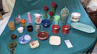 Full view of assorted colorful decor items including pitchers, vases, candleholders, figurines, plates and bowls on a green fabric backdrop.