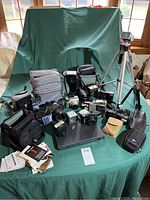 Wide view of all assorted photography gear on green cloth with cases, cameras, flashes, tripod visible.