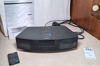 Bose Wave Radio AWR1-1W unit with remote and manual visible in background, cords attached.