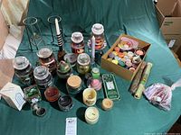 Top-down photo showing a variety of jar candles, tealight candles in a box, candle holders including metal stands and decorative small holders, plus incense sticks and accessories.