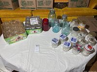 Wide view of the assortment of vintage and new Ball and Atlas canning jars on a table, showing various sizes, some with lids and some without, including a new boxed set.