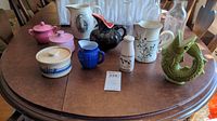 Wide view of all ceramic and glass pieces on table including pitchers, sugar bowls, creamer, and milk bottles