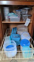 Plastic food storage containers arranged in a kitchen cabinet shelf, showing various sizes and shapes primarily in clear plastic with blue lids and stains on some containers.