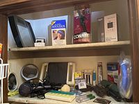 Shelf photo showing assorted health and beauty items including hairdryers, curling irons, lighted mirror, boxed blood pressure monitor, sinus pack, and other small devices.