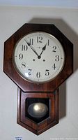 Front view of the wooden octagonal wall clock with visible white clock face, black numerals, and clock hands.