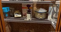 Kitchen shelf with Swirlio frozen dessert maker box, Krups coffee grinder, Rival crockpot with floral design, and Braun coffee maker