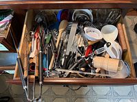 Photo showing drawer filled with assorted kitchen utensils of various materials and colors including wood, metal, and plastic.