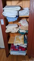 Shelves with multiple folded tablecloths, towels, and linens in various colors including white, blue, cream, beige, and colorful plaid.