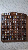 Full view of wooden wall-mounted case with many thimbles displayed in individual compartments under glass.