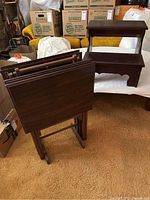 Four wooden TV tray tables stacked upright with a dark wood finish and folding legs, shown next to the step stool.