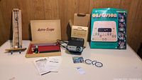 Overview showing all items clearly: wooden Astro-Scope telescope model with balls, View-Master projector and disks, Obsession game box, and Gravitation game surface