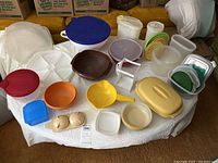 Photo showing large assortment of vintage Tupperware items on a table including bowls, storage containers with lids, strainer bowls, and a butter dish.