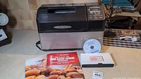 Zojirushi breadmaking machine with associated manuals and a CD placed in front of it on a kitchen counter.