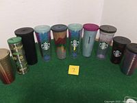 Full view of 10 Starbucks containers with various colors, patterns, and lids including green, black, purple, turquoise, and multi-color designs.