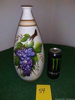 Front view of the ceramic vase with hand-painted grape cluster and leaves, placed next to a soda can for scale.