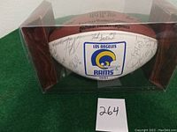 Football displayed in clear display case showing Rams logo and multiple autographs on white panel.