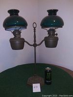 Complete antique double oil lamp with green glass shades on a green surface with a Monster energy drink can for scale.