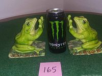 Pair of green ceramic frog bookends positioned with a Monster energy drink can for scale on green fabric.