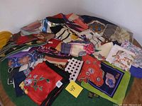 Photo showing a collection of folded vintage scarves with various patterns on a surface, highlighting multiple colors and different designs including a red scarf with floral embroidery and a scarf with polka dots.